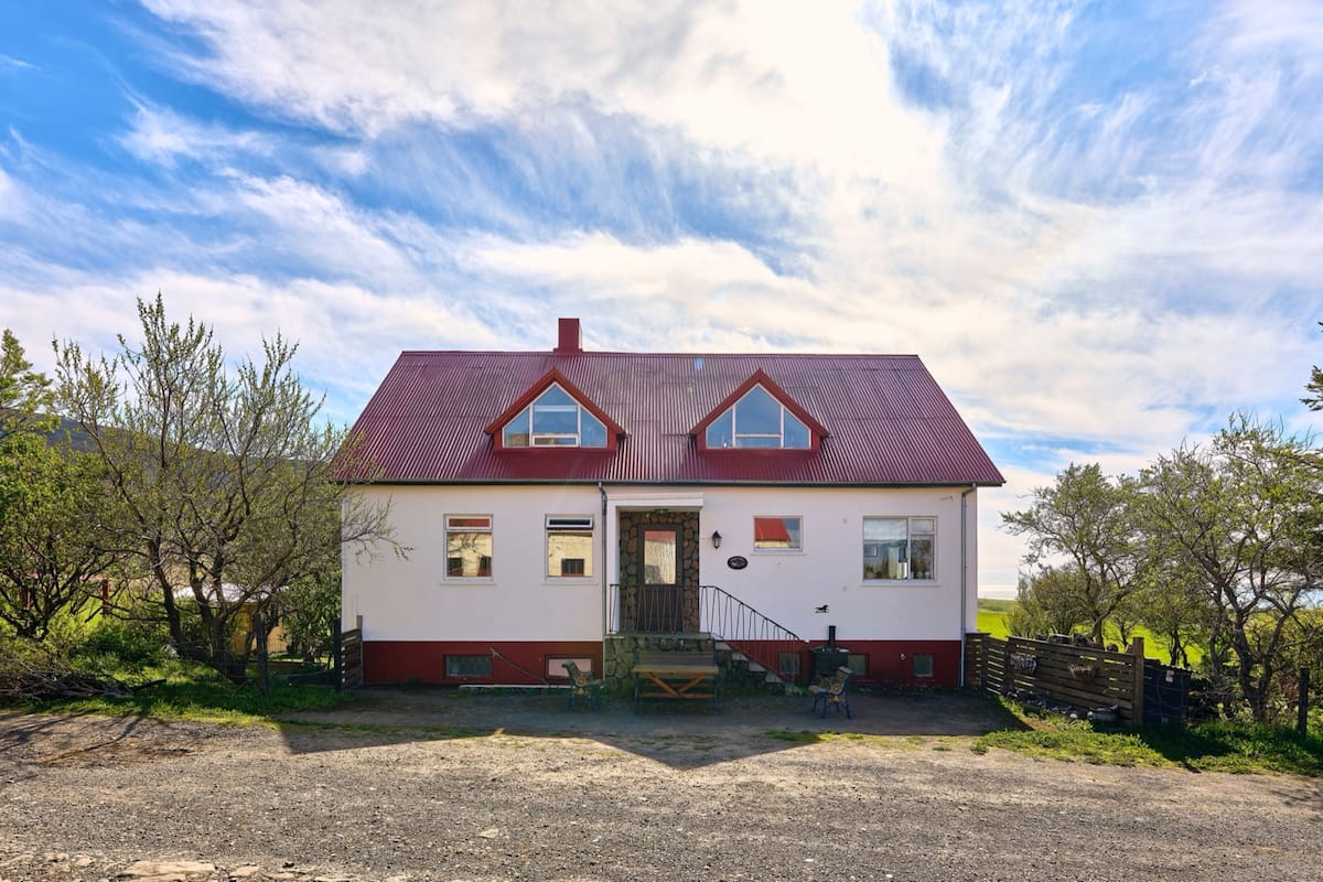 A two-story house with a red roof, a stone staircase, and a wooden fence.
