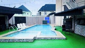 A swimming pool with a stone border, surrounded by artificial grass and a stone wall. - Mo-House Hotels and Events Centre (Abuja)