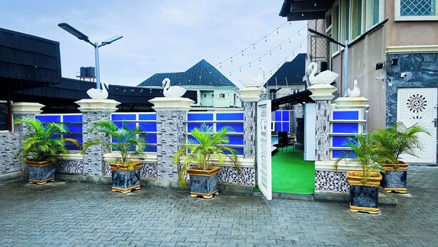 A gated entrance with blue-framed windows, potted plants, and a green artificial turf pathway. - Mo-House Hotels and Events Centre (Abuja)