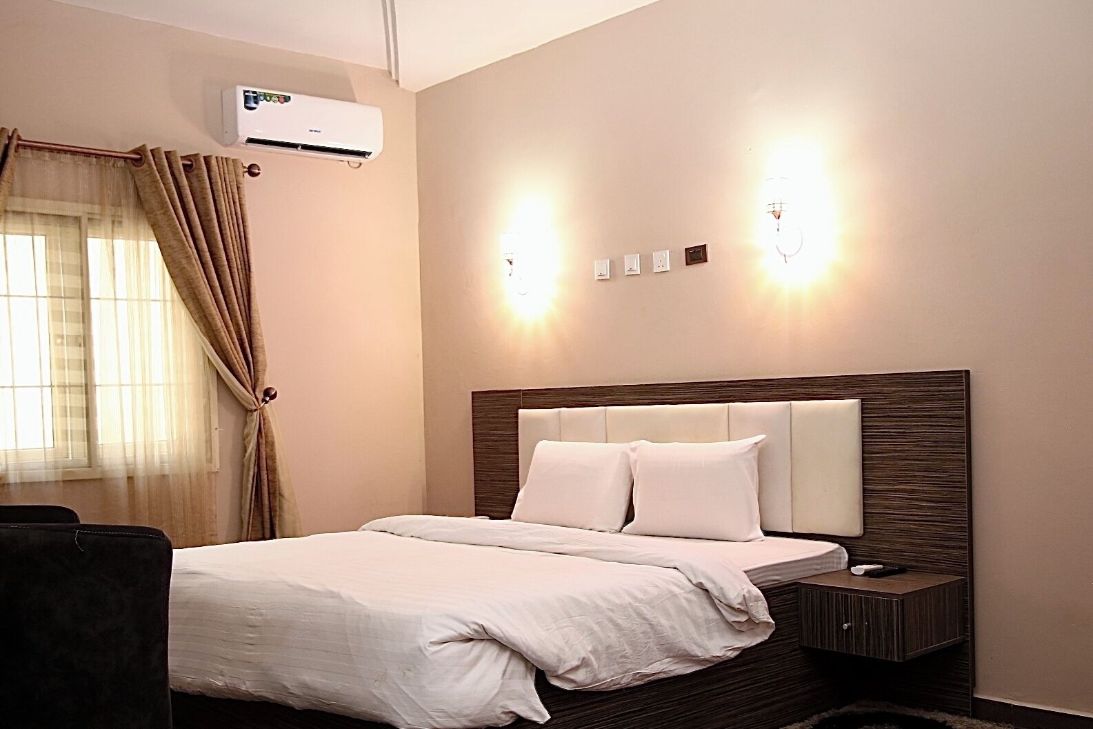 Ein Hotelzimmer mit Bett, Nachttisch, Klimaanlage und Wandleuchten.