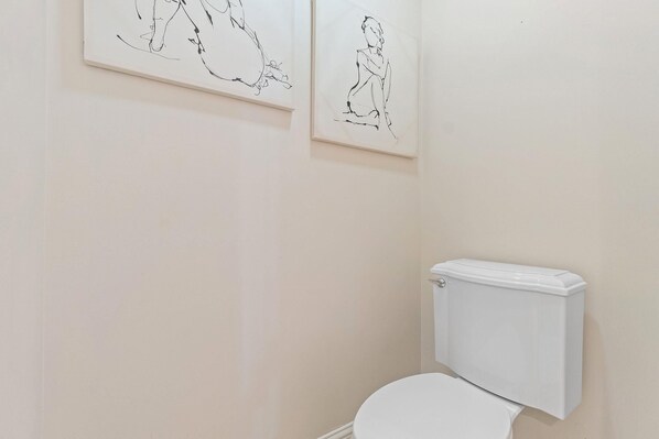A bathroom with a toilet and two line drawings on the wall. - The Wharf 403 (Orange Beach)