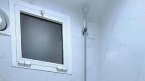 Un baño pequeño y blanco con inodoro, ducha y ventana sobre el inodoro.