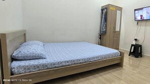 Ein Einzelbett mit Holzrahmen und gemustertem Lattenrost, ein Holfschrank, ein an der Wand befestigter Fernseher und ein kleiner Hocker.