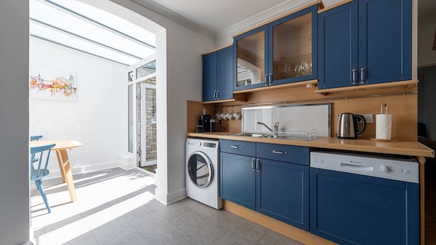 A modern kitchen with blue cabinets, a washing machine, a dishwasher, and a coffee maker. - GuestReady - 2bed Battersea flat with Patio (London)