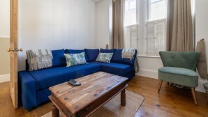 A living room with a blue sofa, a wooden coffee table, and a green armchair. - GuestReady - 2bed Battersea flat with Patio (London)
