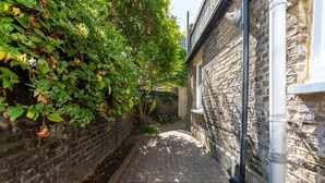A narrow brick alleyway with a stone wall on one side and a building on the other. - GuestReady - 2bed Battersea flat with Patio (London)