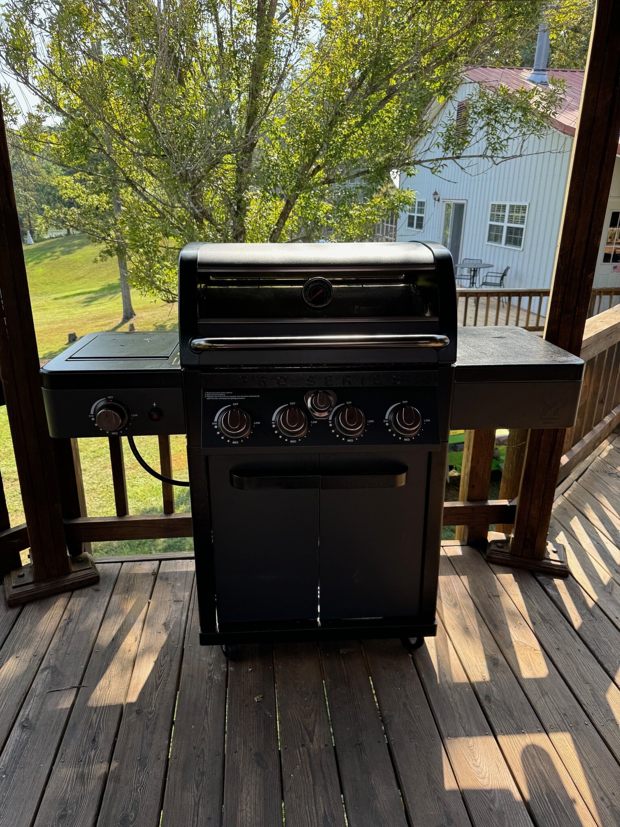 A black outdoor grill on a wooden deck with a view of a house and trees in the background.