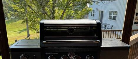 A black outdoor grill on a wooden deck with a view of a house and trees in the background.