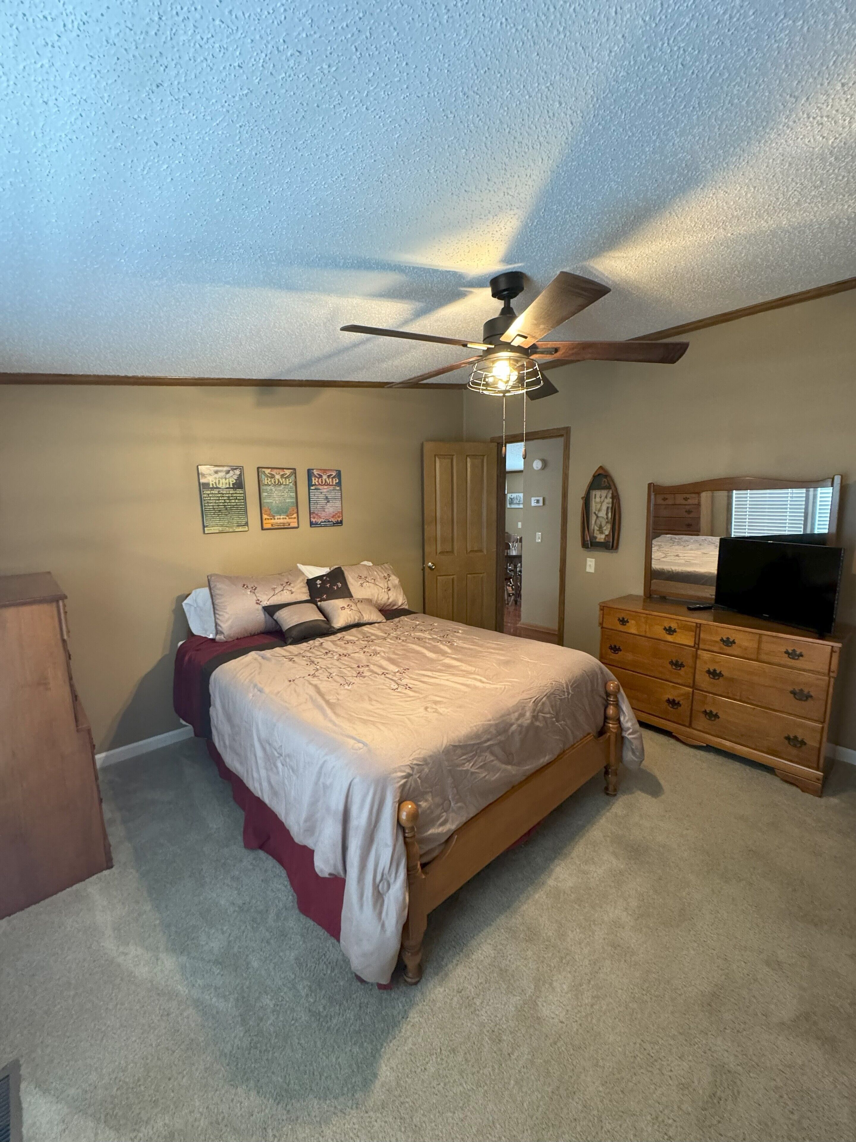 A bedroom with a bed, dresser, ceiling fan, and wall decorations.