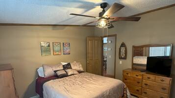 A bedroom with a bed, dresser, ceiling fan, and wall decorations.
