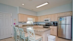 A kitchen with light wood cabinets, a stainless steel refrigerator, a microwave, and a granite countertop.