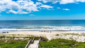 A beach with a wooden boardwalk leading to the shore, clear skies, and a calm sea.
