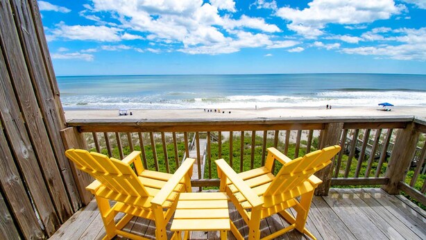 A wooden deck with yellow Adirondack chairs and a view of the beach.