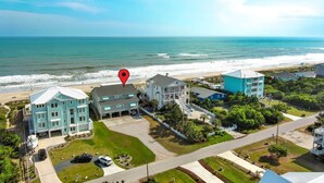 An aerial view of a coastal residential area with beachfront properties, including a multi-story building with balconies and a blue building with a white roof.