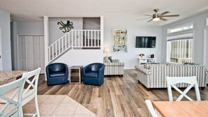 A spacious living room with a staircase, a dining area, and a seating area with a sofa and chairs.