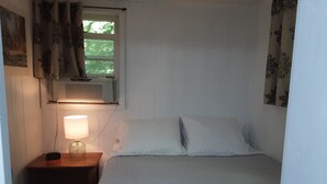 A bedroom with a bed, a nightstand with a lamp, a window with curtains, and an air conditioning unit. - Newly Renovated Cabin on a Private Lake Great for a Romantic Getaway or some R&R (Second Eel River Lake)