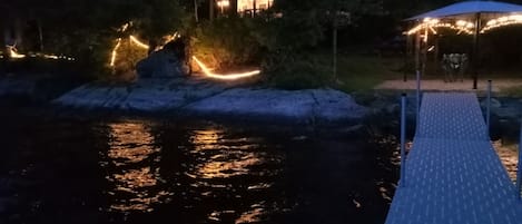 A wooden dock extending into a body of water with a gazebo and a building with lights in the background.