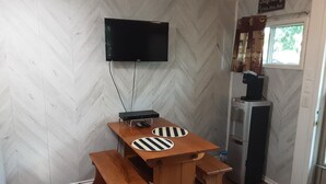A compact kitchen with a wooden table, two benches, a flat-screen TV mounted on the wall, and a refrigerator. - Newly Renovated Cabin on a Private Lake Great for a Romantic Getaway or some R&R (Second Eel River Lake)