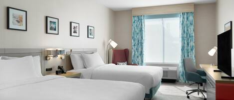 A hotel room with two beds, a desk, a chair, a TV, and a window with curtains.