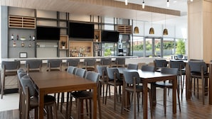 A modern restaurant with a bar area, multiple seating options, and a large TV screen. - Hilton Garden Inn Austin Central (Austin)