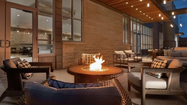 An outdoor seating area with wicker furniture, a central fire pit, and large windows. - Hilton Garden Inn Austin Central (Austin)