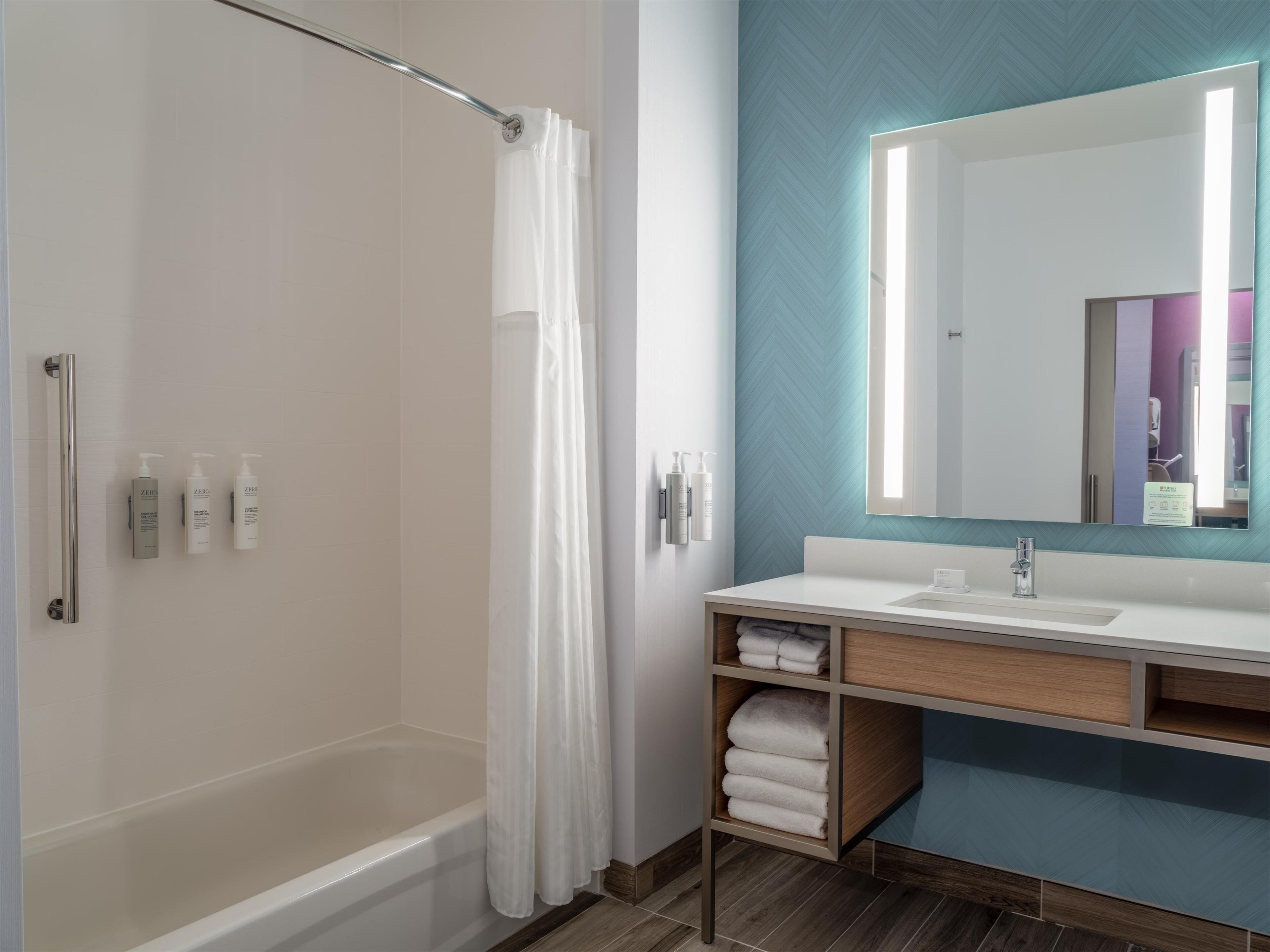 Een moderne badkamer met een bad, douchegordijn, wastafel en spiegel, en toiletartikelen aan de wand.