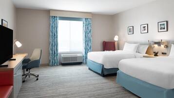 A hotel room with two beds, a desk, a chair, and a TV.