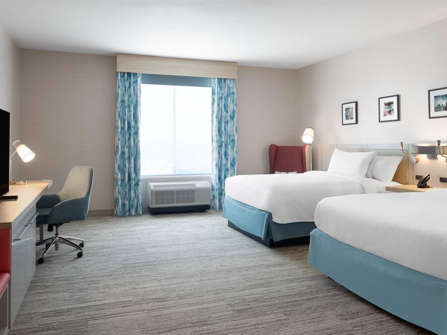 A hotel room with two beds, a desk, a chair, and a TV.