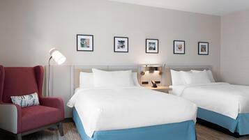 Een hotelkamer met twee bedden, een rode fauteuil, een vloerlamp en vier ingelijste foto's aan de muur.