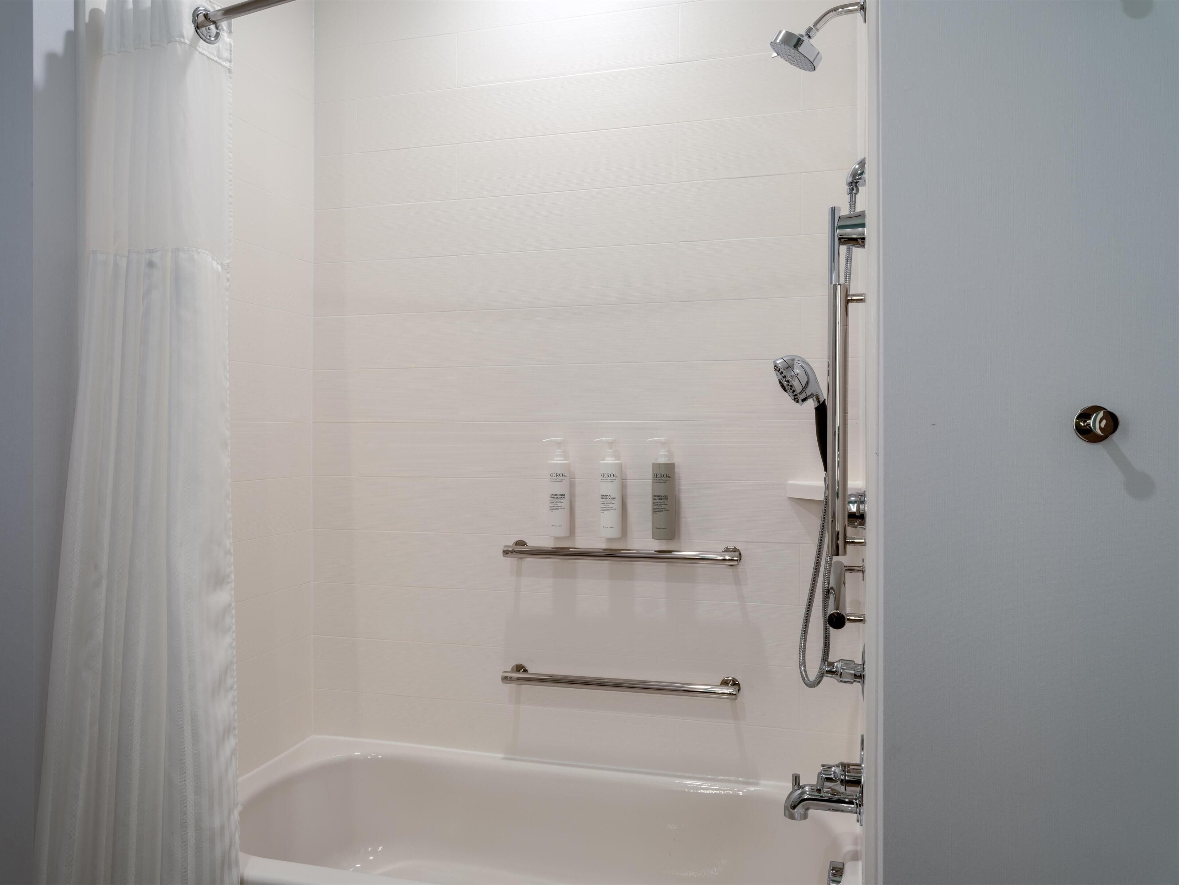 A modern bathroom with a bathtub, shower, and handrails.