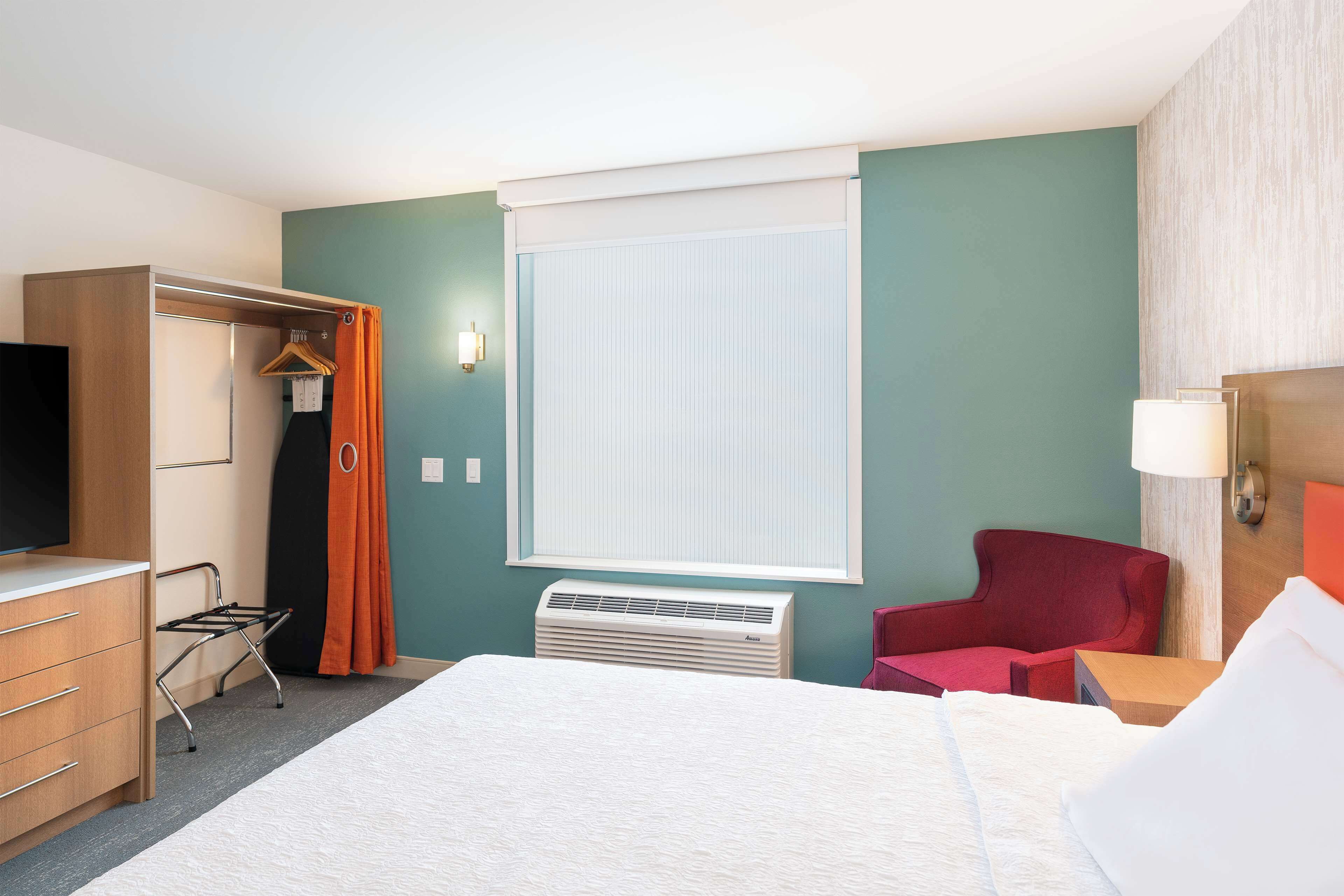 A hotel room with a bed, a wardrobe, a chair, a desk, and a television.