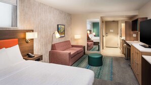 A hotel room with a large bed, a sofa, a desk with a computer, a TV, and a bathroom visible through an open door. - Home2 Suites by Hilton Bozeman Midtown (Bozeman)
