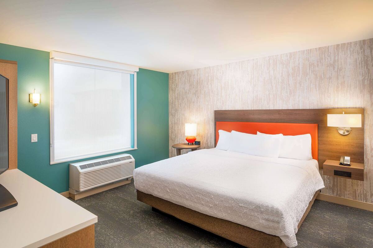 Habitación de hotel con una cama grande, un escritorio, una ventana con persianas, un calentador y dos lámparas de noche.