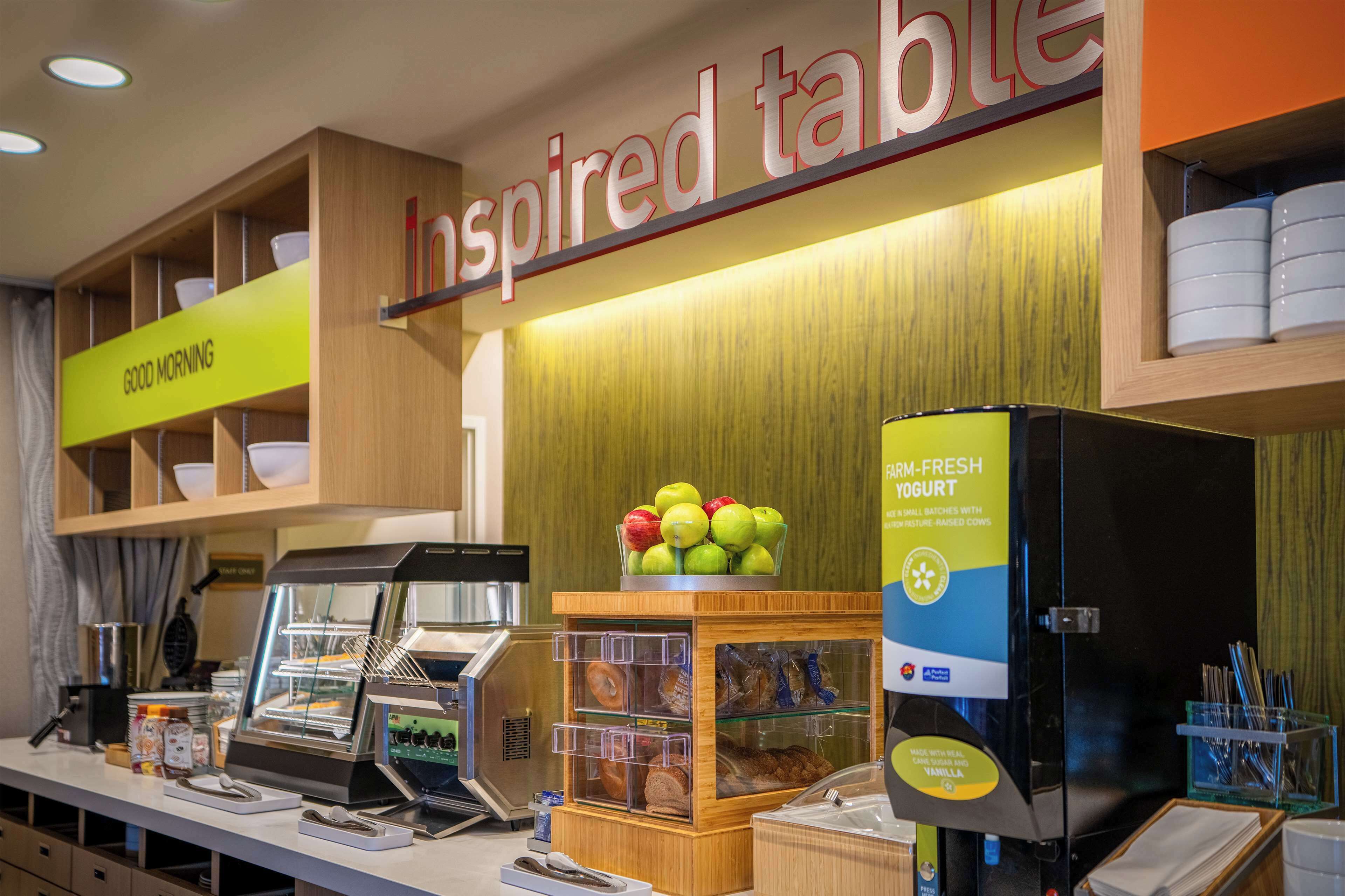 Un espace dédié au petit-déjeuner, avec un buffet où les clients peuvent se servir eux-mêmes, une présentation de fruits frais et un panneau indiquant « Table d’inspiration ».