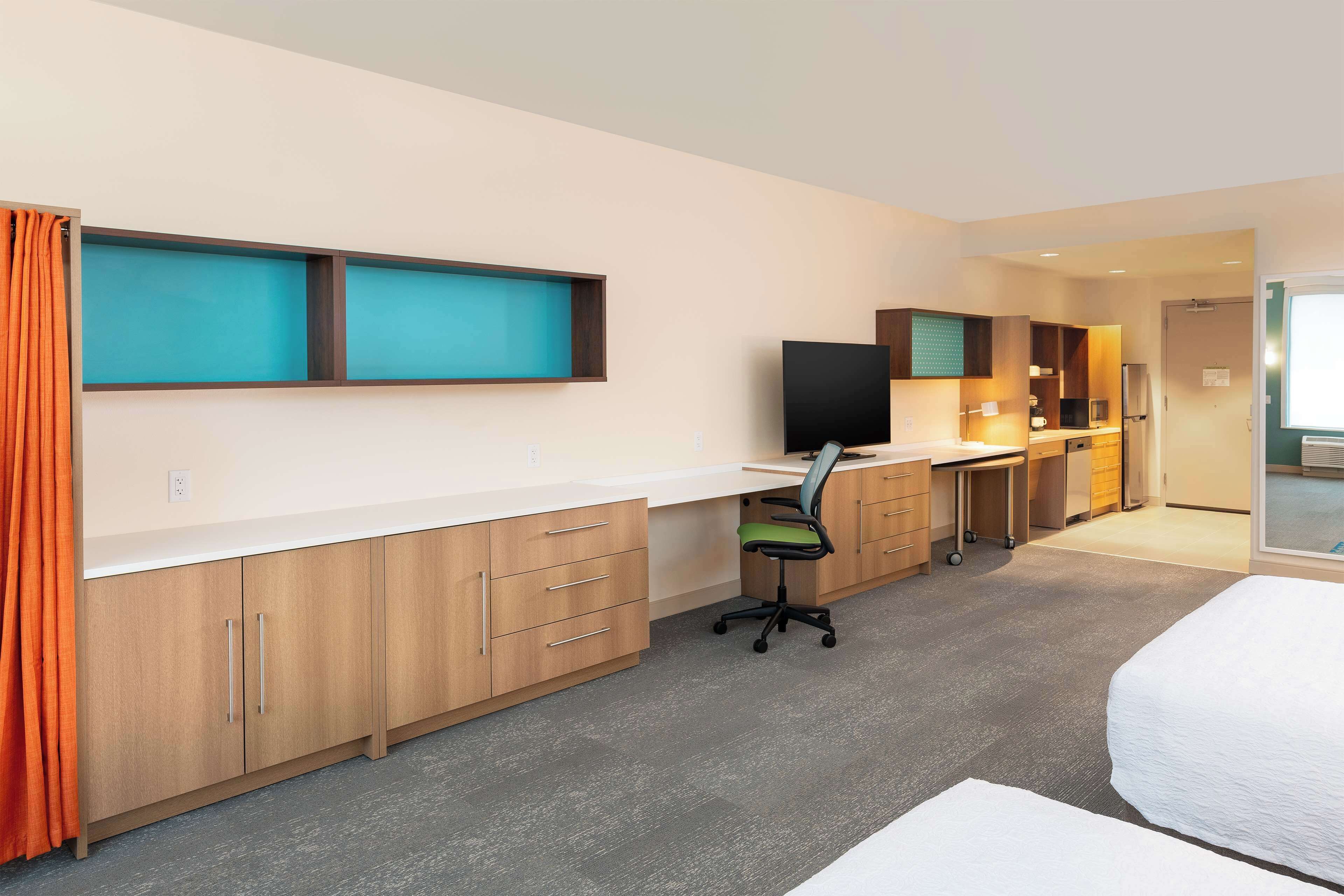 A hotel room with a bed, a desk with a chair, a television, and a kitchenette.