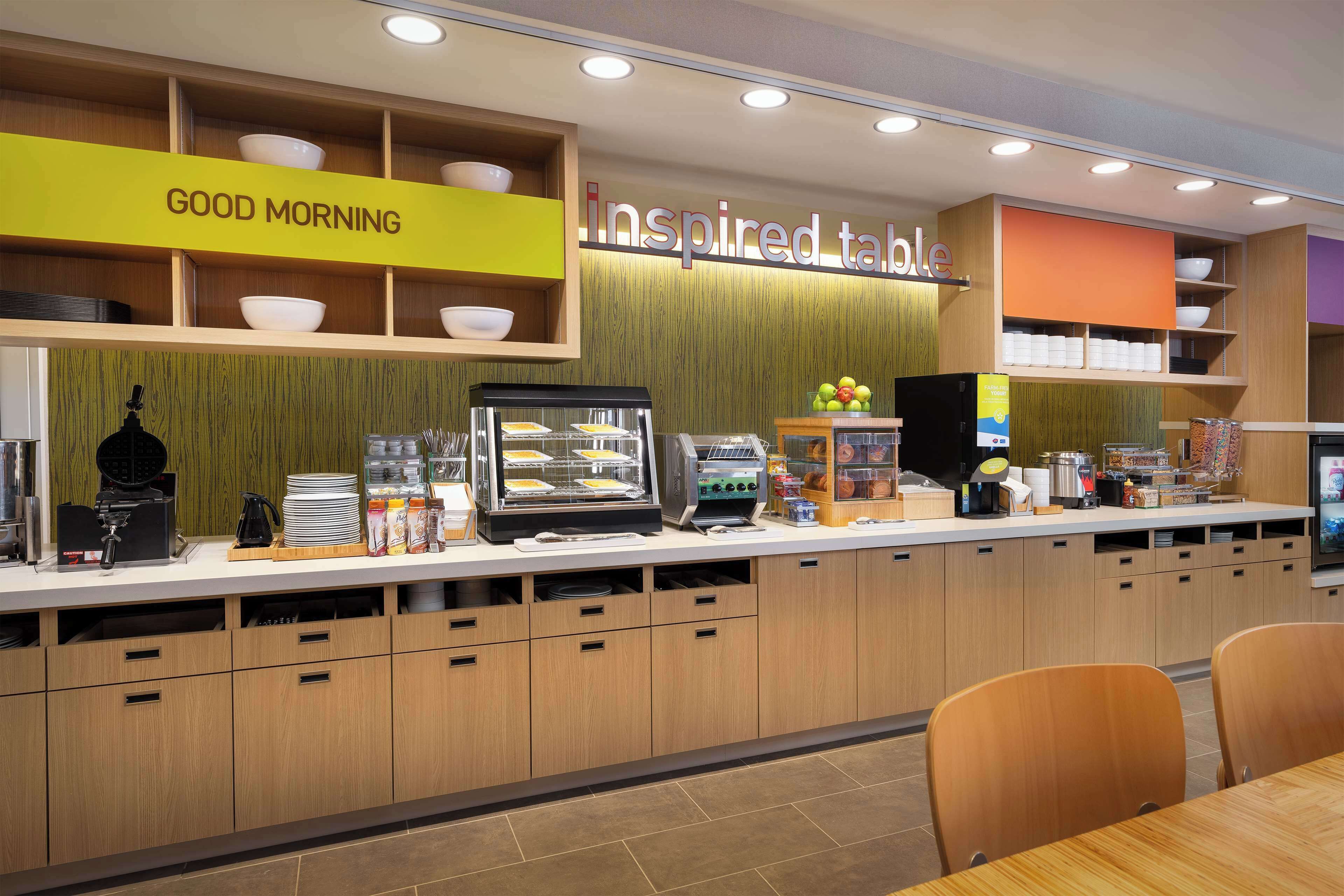 A breakfast bar with a 'Good Morning' sign, a display case with food items, and a 'Inspired Table' sign.