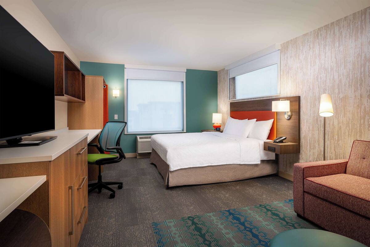 Una habitación de hotel con cama, escritorio con computadora, silla, televisor y ventana.