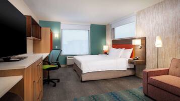 Ein Hotelzimmer mit Bett, Schreibtisch, Computer, Sessel, Fernseher und Fenster.