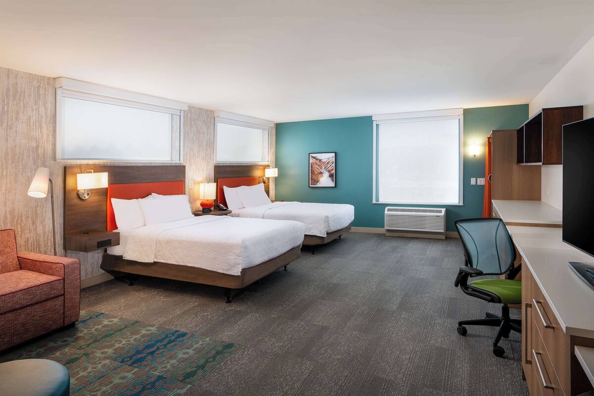 Habitación de hotel con dos camas, un escritorio, una silla, un televisor y una ventana.