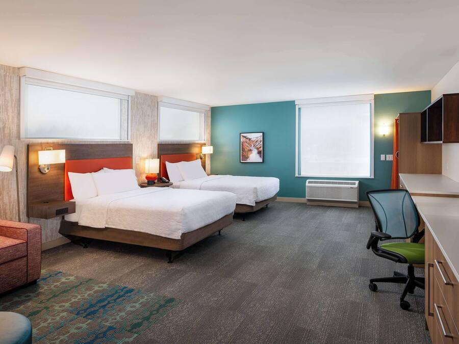 A hotel room with two beds, a desk, a chair, a TV, and a window.