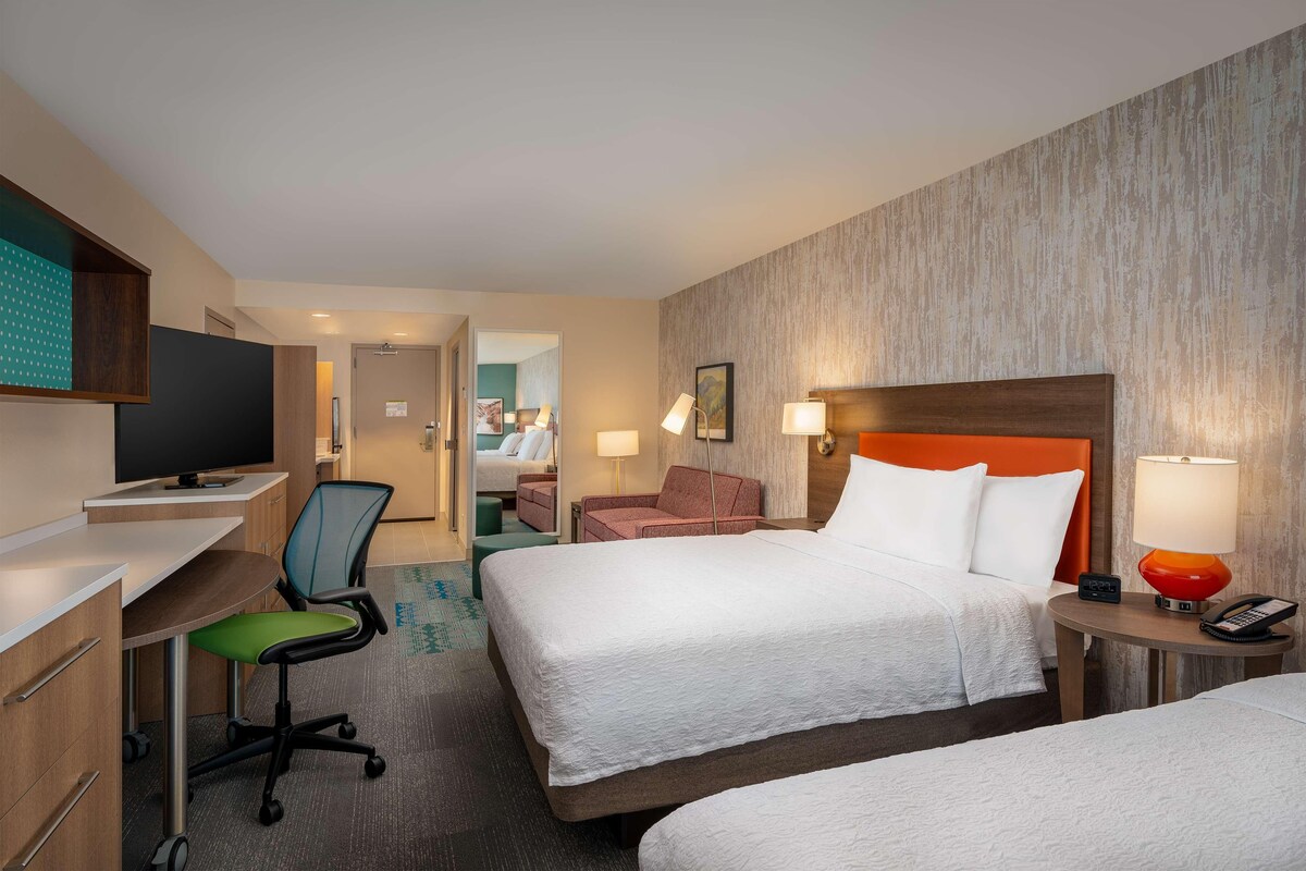 Une chambre d’hôtel avec deux lits, un bureau, une chaise, une télévision et une lampe.