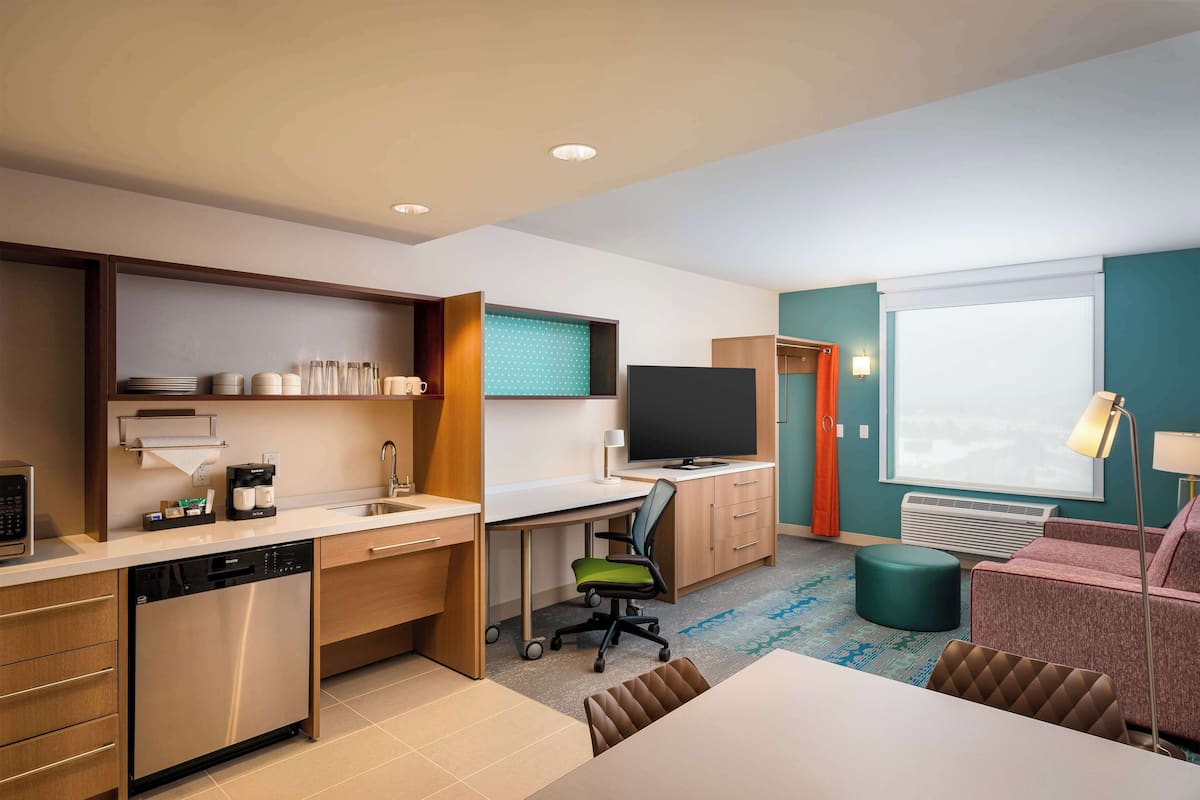 Habitación de hotel pequeña con kitchenette, televisión de pantalla plana, sofá y zona de comedor.