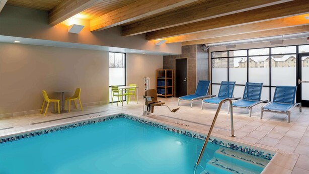 An indoor swimming pool with a wooden ceiling, yellow chairs, and blue lounge chairs. - Home2 Suites by Hilton Bozeman Midtown (Bozeman)