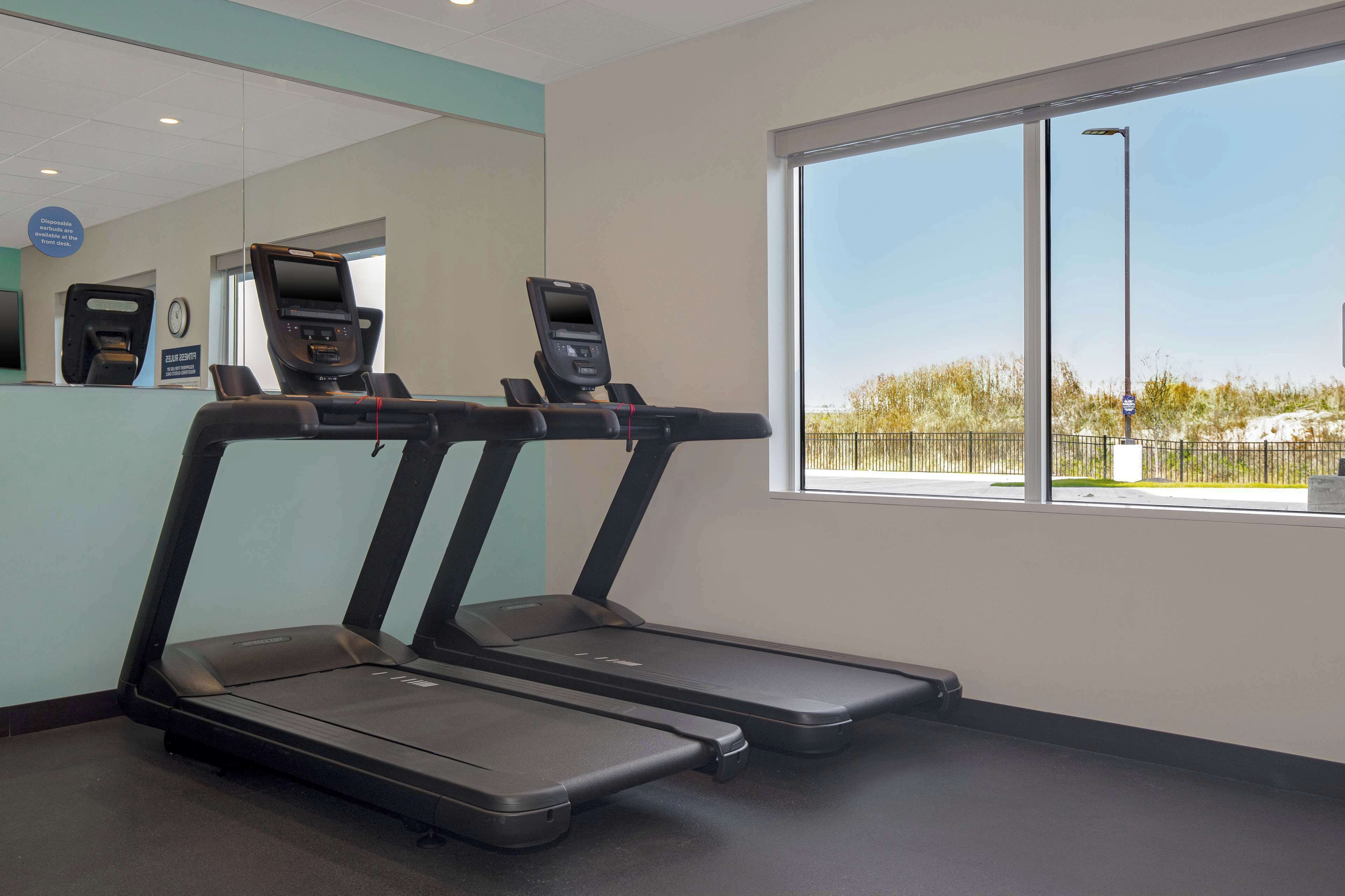 Une salle de sport équipée de tapis de course, d’un comptoir d’accueil et d’une grande fenêtre donnant sur un espace clos.