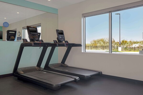 A gym with treadmills, a reception desk, and a large window with a view of a fenced area.