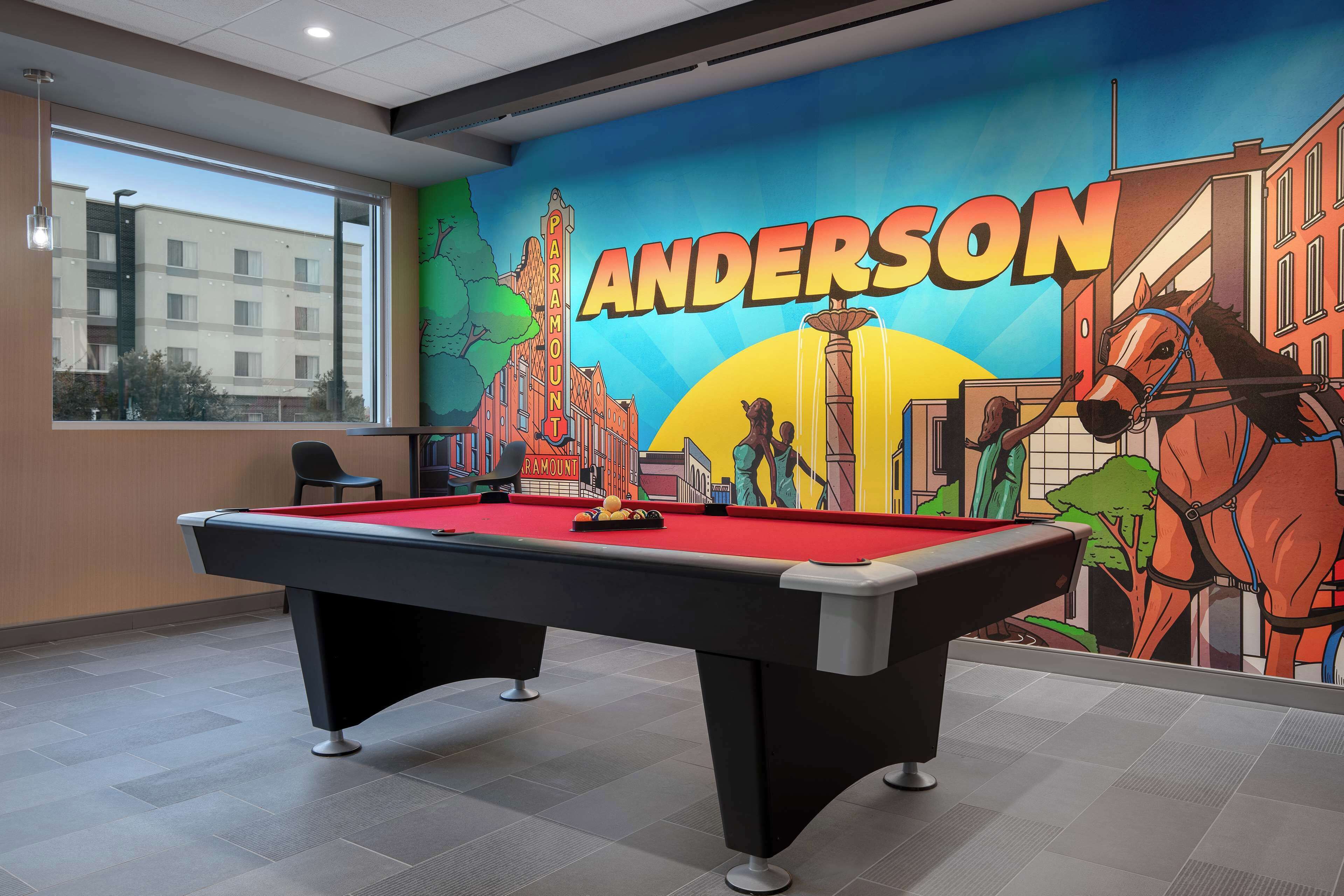 Uma mesa de bilhar em um salão com um mural de um cavalo e a palavra "ANDERSON" na parede.