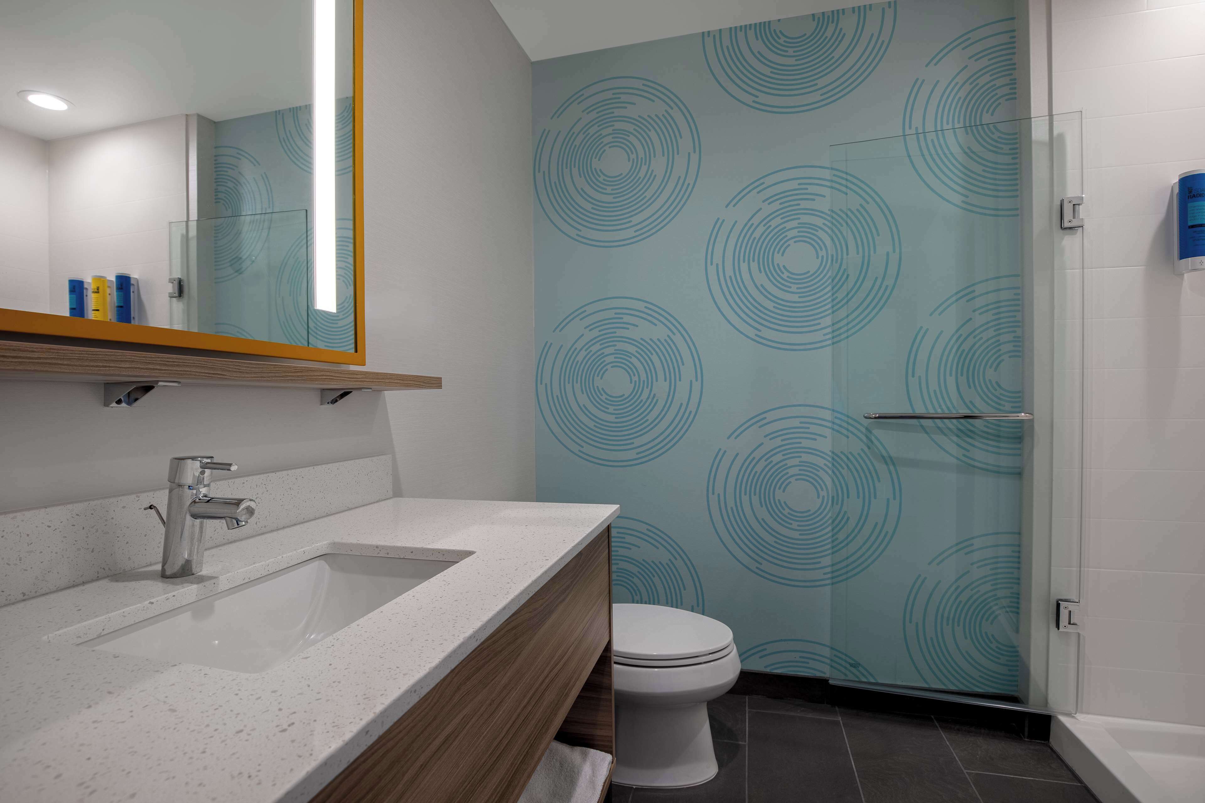 Un baño moderno con lavamanos, espejo e inodoro blancos.