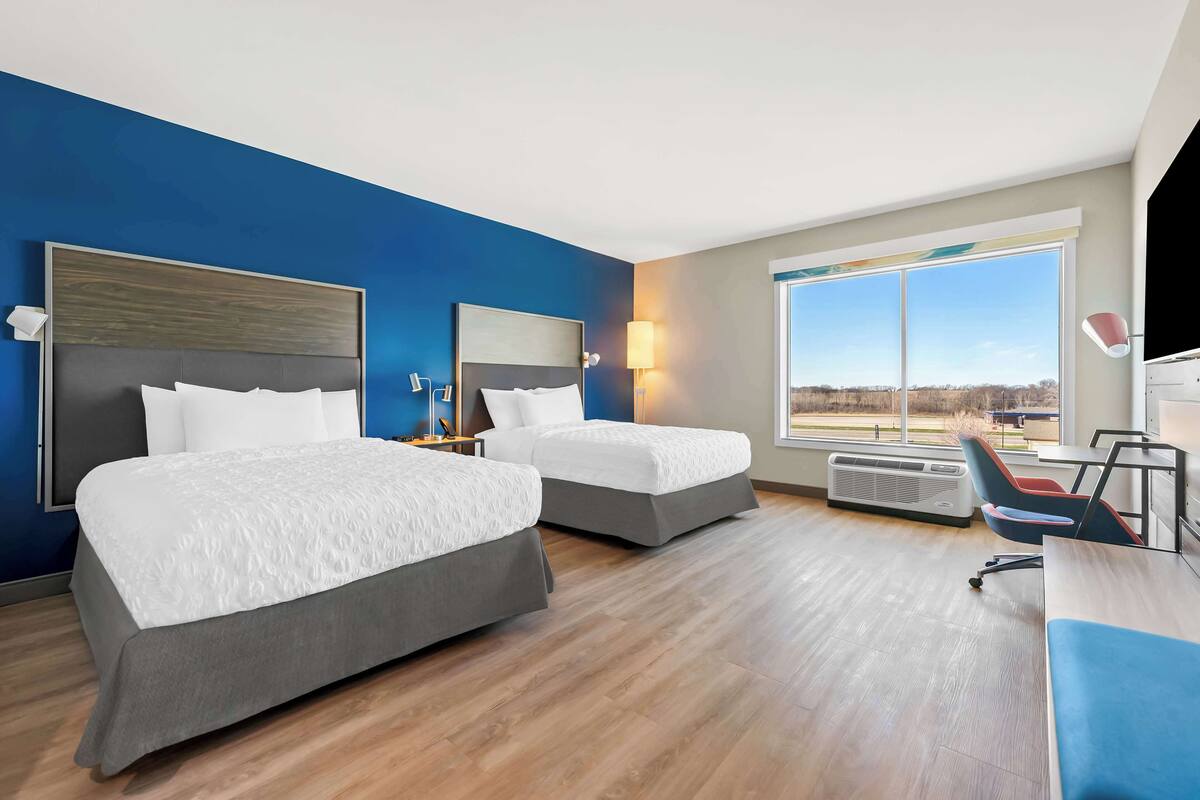 A hotel room with two beds, a desk, a chair, a large window, and a view of the outdoors.