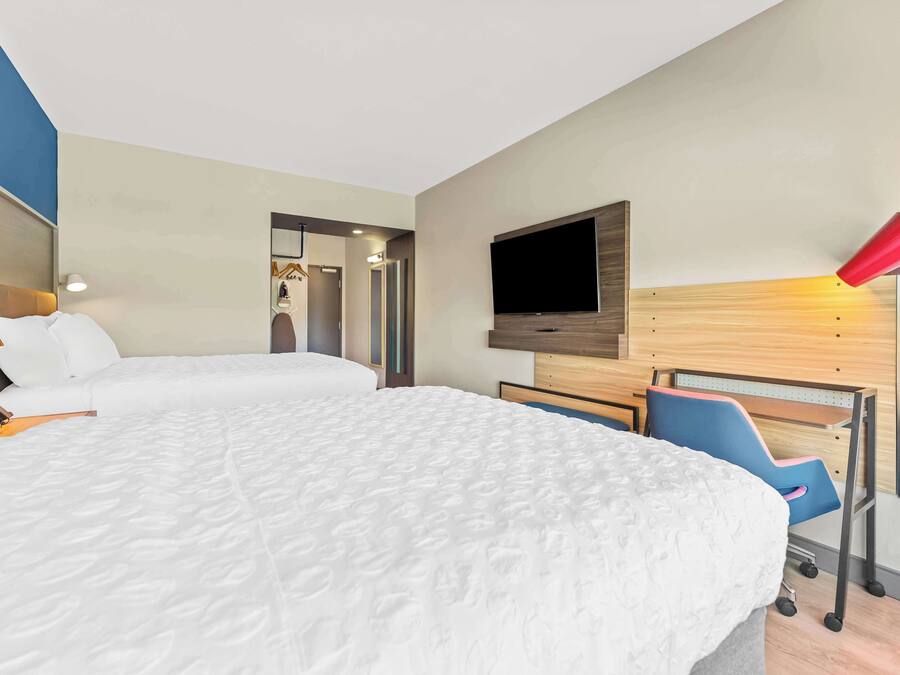 A hotel room with two beds, a TV, a desk with a chair, and a red lamp.