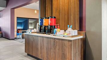 Una moderna zona de recepción con mostrador de madera, dispensadores de café y un área de descanso al fondo.